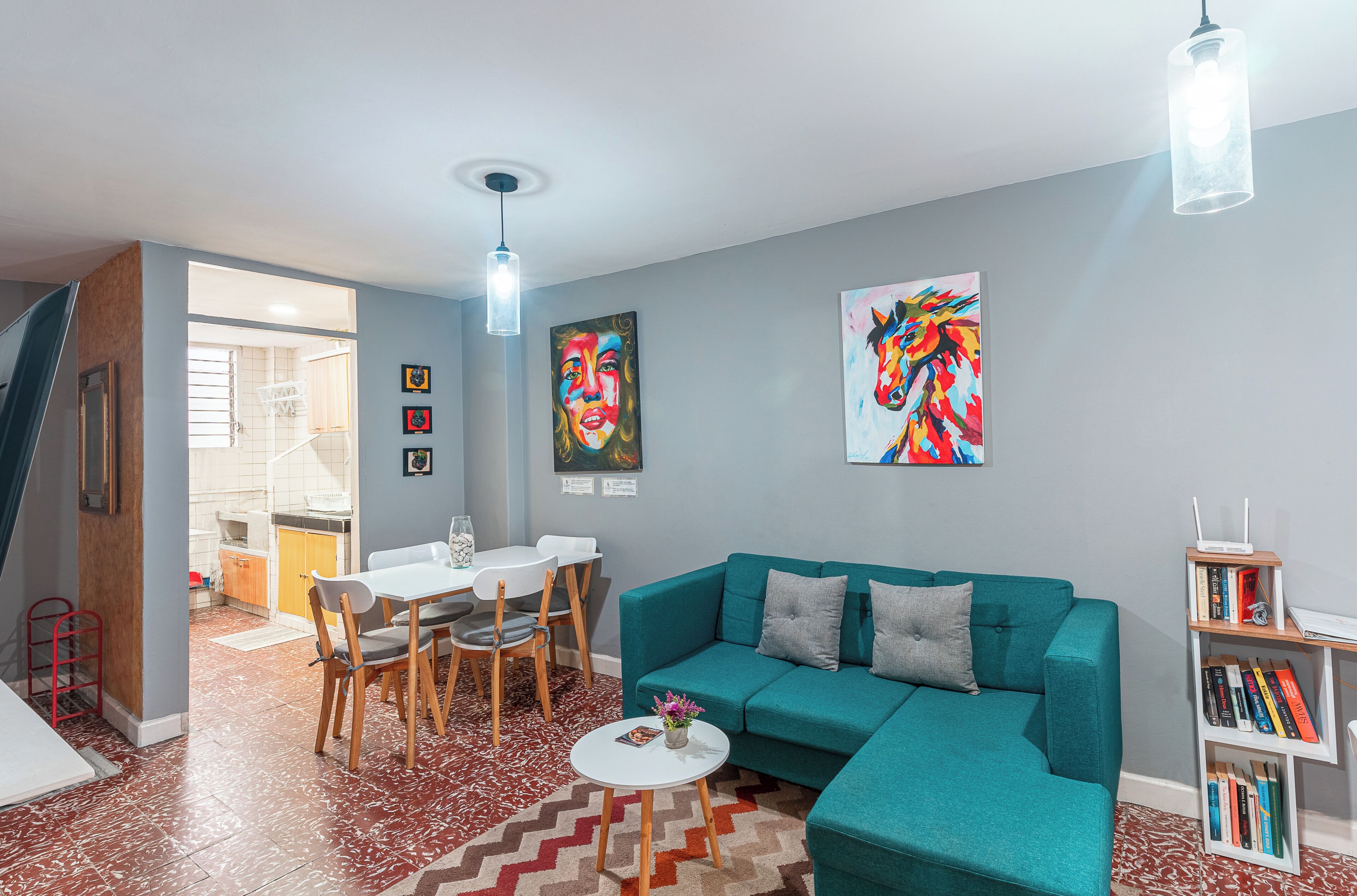 Un salon moderne avec un canapé de couleur turquoise, une table à manger avec des chaises, une petite table basse blanche et une bibliothèque.