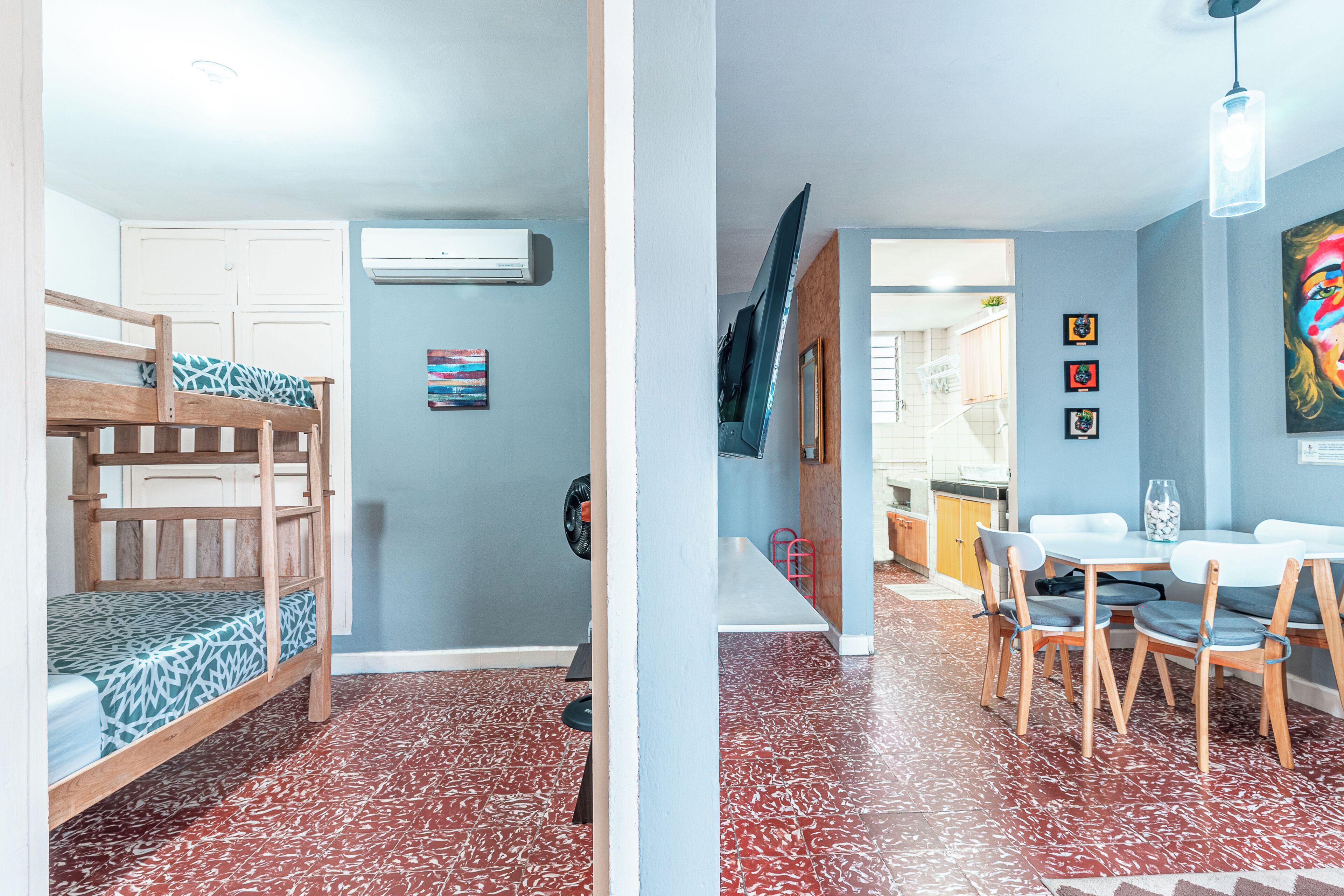 A room with a bunk bed, a dining table with chairs, and a kitchen area visible through an open door.