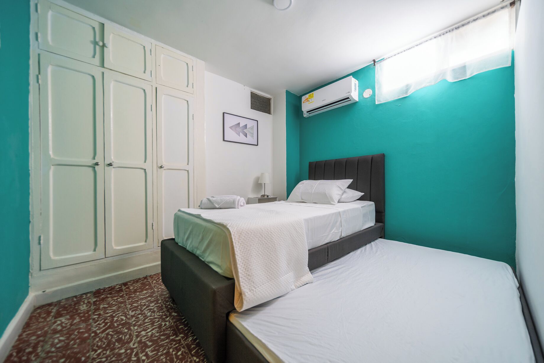 A bedroom with a bed, a wardrobe, a nightstand, an air conditioner, and a window with a curtain.