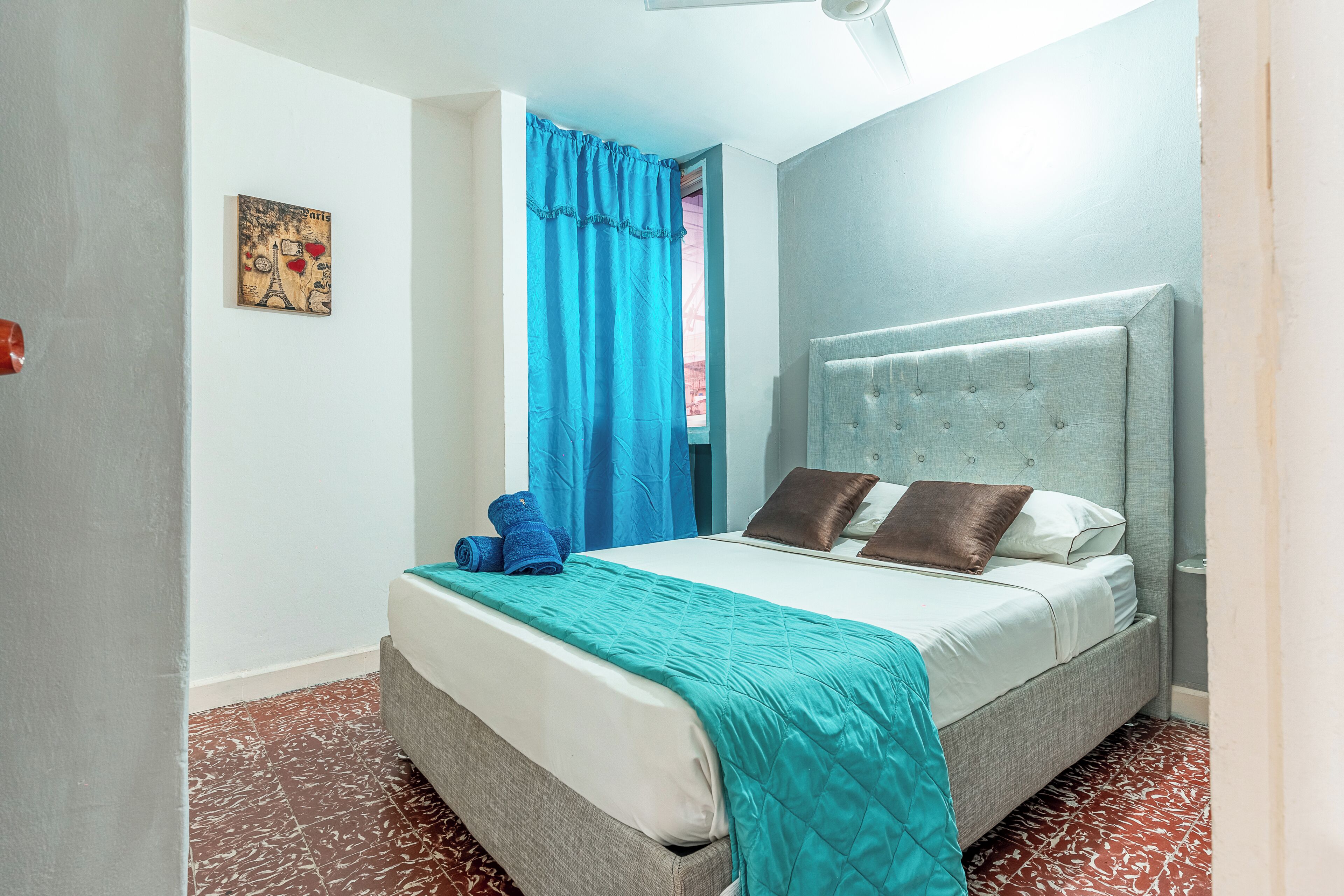 Une chambre à coucher avec un lit, une tête de lit, un rideau bleu et un tableau accroché au mur.