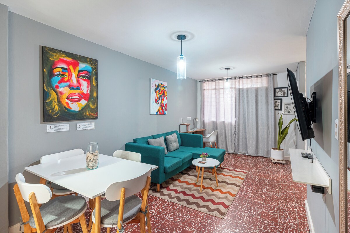 Un saló modern amb un sofà color turquesa, una taula de dinar blanca i una televisió penjada a la paret.