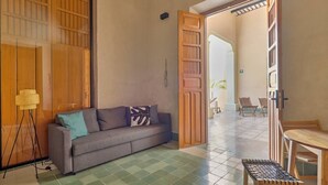 Une pièce comprenant un canapé, une petite table et une chaise. Une porte donne accès à une autre pièce.