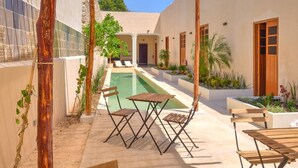 Un espace aménagé au bord de la piscine, avec une pergola, des sièges et une vue sur un bâtiment doté d’une porte et de fenêtres.