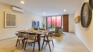 A modern living room with a dining area, a flat-screen TV, and a large window with a view.