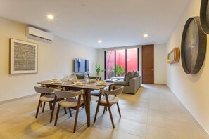 A modern living room with a dining area, a flat-screen TV, and a large window with a view. - Casa Chak K`u | 2 bd | 2.5 bth | private pool (Merida)