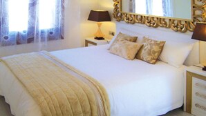 A neatly made bed with a white comforter and a beige throw blanket, a bedside lamp, and a mirror with a decorative frame. - Torre del Sol Charming Vacation Home (Guia de Isora)