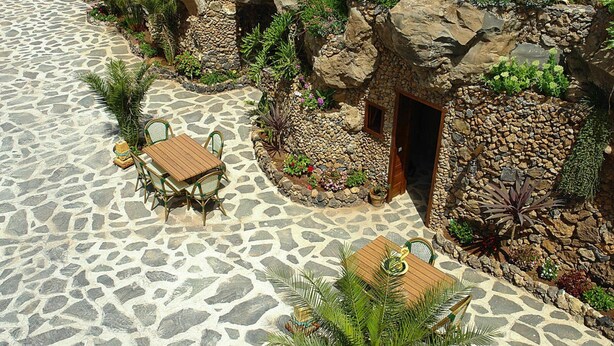 A stone patio with a wooden table and chairs, surrounded by a rock garden with various plants. - Torre del Sol Charming Vacation Home (Guia de Isora)