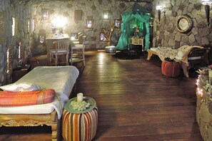 A room with a stone wall, wooden floor, a bed with a red pillow, a table with chairs, and a green curtain. - Torre del Sol Charming Vacation Home (Guia de Isora)