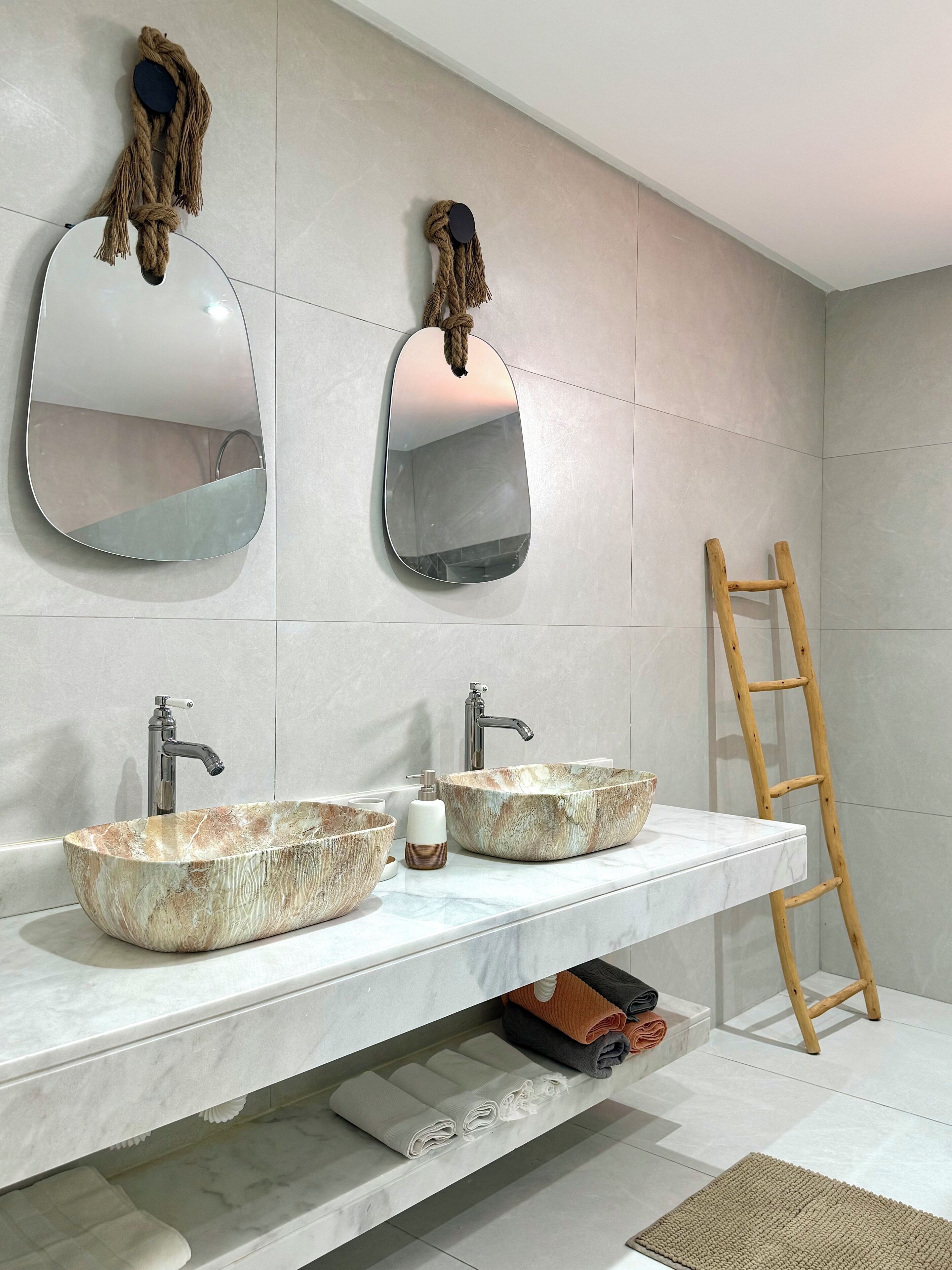 A bathroom with two round, marble sinks, a wooden ladder, and a towel rack.