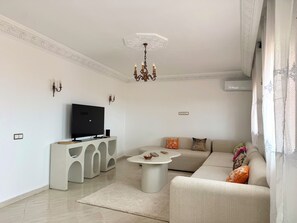 Ein modernes Wohnzimmer mit Fernseher, weißem Sofa, Couchtisch und einer Kronleuchter.