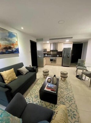 A living room with a sofa, coffee table, and ottoman, a kitchen with cabinets and appliances, and a painting on the wall. - Cozy apartment in the heart of Guayaquil (Guayaquil)