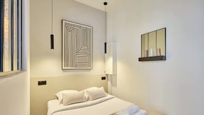 Een moderne hotelkamer met een net opgemaakt bed, een geometrisch kunstwerk aan de muur, een spiegel met plankje en een hanglamp.