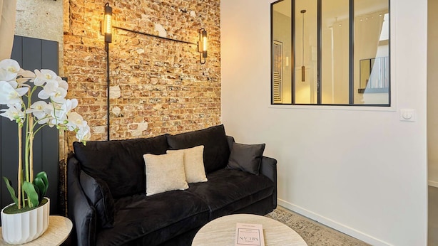 Een moderne woonkamer met een bakstenen muur, een zwarte leren bank, een ronde salontafel en een orchidee in een pot.