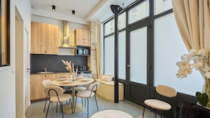 Een moderne keuken met houten kasten, een zithoek met ronde tafels en stoelen, en een groot raam met gordijnen.