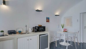 A compact kitchenette with a sink, microwave, kettle, and a small refrigerator. There is a dining area with a table and chairs. - Fira Retreat With Sea Views (Santorini)