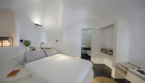 A modern bedroom with a large bed, bedside lamps, and a small table with books and a lantern. - Fira Retreat With Sea Views (Santorini)
