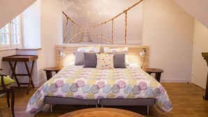 Ein Schlafzimmer mit einem Bett, einem Holztisch, einem Stuhl und einem Kunstwerk mit einer Seilbrücke an der Wand.
