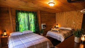 Een houten kamer met twee bedden, een houten dressoir, een kachel en een raam met groene gordijnen.