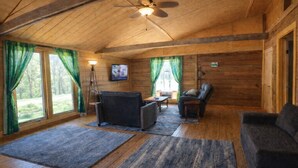 Een blokhut interieur met een plafondventilator, een televisie, een open haard en een bank.