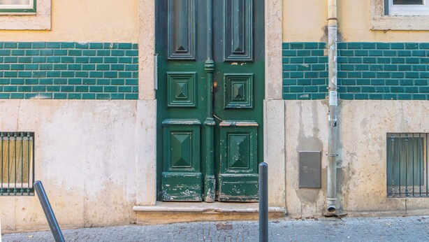 Un immeuble avec une porte verte, un balcon doté d’une rambarde en métal et une fenêtre avec un volet.