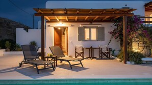 Un área junto a la piscina con sillones de descanso, una mesa y una pérgola.