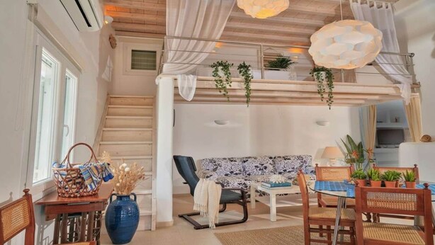 Una habitación amplia con una escalera, un sofá, una mesa de comedor y plantas colgantes.