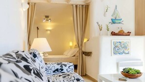 Habitación de hotel con cama, sofá, lámpara, estante empotrado con adornos y vistas a través de una cortina.
