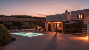Una villa moderna con piscina, mobiliario exterior y un muro de contención de piedra.