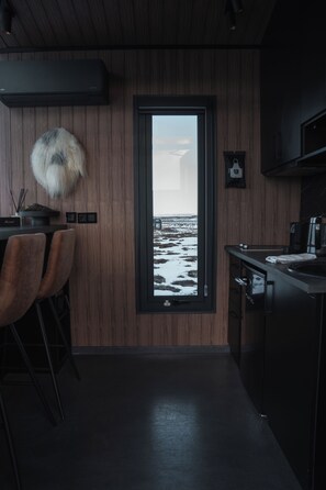 A modern kitchen with a view of a snowy landscape through a large window. - Tiny Glass lodge Experience The Nature (Selfoss)