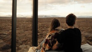 A room with a large window overlooking a barren landscape with mountains in the distance. - Tiny Glass lodge Experience The Nature (Selfoss)