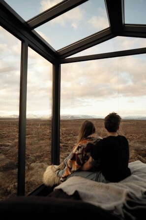 A room with a large window overlooking a barren landscape with mountains in the distance. - Tiny Glass lodge Experience The Nature (Selfoss)