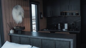 A modern bedroom with a large bed, a small kitchenette, and a view of the outdoors. - Tiny Glass lodge Experience The Nature (Selfoss)