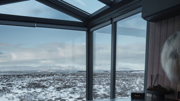 A modern kitchen with a large window, two bar stools, and a view of a snowy landscape. - Tiny Glass lodge Experience The Nature (Selfoss)
