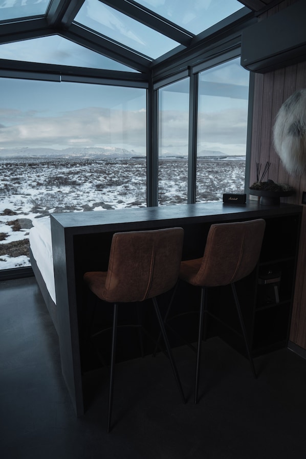 A modern kitchen with a large window, two bar stools, and a view of a snowy landscape. - Tiny Glass lodge Experience The Nature (Selfoss)