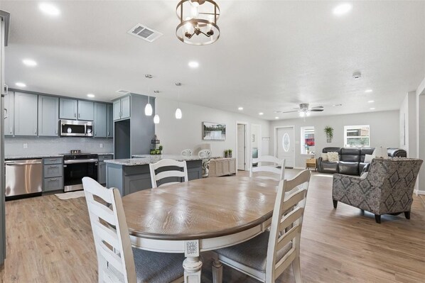 A spacious kitchen with modern appliances, a dining area with a wooden table and chairs, and a living area with a sofa and armchair. - Waterfront-Fishing-Kayaking-Long or Short Stays-4 Bedroom 3 Bath-Gameroom (Granbury)