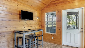 Ein Zimmer mit Holzpaneelen, einem an der Wand montierten Fernseher, einem Fenster mit Jalousien und einer weißen Tür.