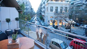 Ein Balkon mit Blumentöpfen, Blick auf eine belebte Straße mit parkenden Autos und Gebäude mit Balkonen.