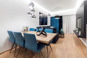 A modern dining area with a wooden table, blue chairs, and a unique light fixture. - Acropolis Museum View Deluxe Apartment | 3 Falirou str 11742 Athens (Athens)