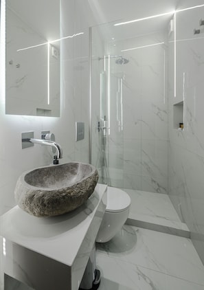A modern bathroom with a stone basin, a toilet, and a glass-enclosed shower area. - Acropolis View  Signature Penthouse (Athens)