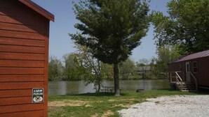 Una cabaña con un letrero que dice 'CABIN PGYCOS' junto a un lago, una mesa de picnic y un árbol.