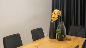 Un espace repas moderne avec une table en bois, des chaises noires, un vase de fleurs et des luminaires suspendus.