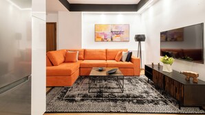 Un salon moderne avec un canapé d’angle, une table basse, un tapis noir, un téléviseur à écran plat et un tableau accroché au mur.