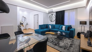 Un salon moderne avec un canapé d’angle bleu, une table à manger en verre et un tapis noir et blanc.