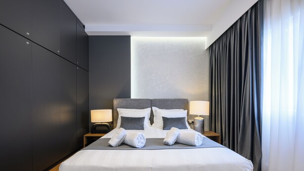 Une chambre d’hôtel moderne avec un grand lit, deux tables de chevet avec des lampes, des rideaux foncés et un plancher en bois.