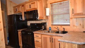 A kitchen with wooden cabinets, a black refrigerator, a stove, a microwave, and a sink. - Waterfront Cottage | Steps from Pine Lake & Resort Amenities | Resort Amenities (Pike County)