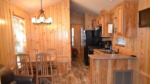 A wooden cabin interior with a dining area, kitchen, and a living space with a couch. - Waterfront Cottage | Steps from Pine Lake & Resort Amenities | Resort Amenities (Pike County)