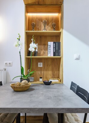 A dining area with a wooden bookshelf, a vase of white orchids, and a bowl of nuts. - Acropolis Golden View Penthouse | 17 Dimitrakopoulou str 11742 Athens (Athens)