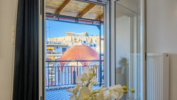 Una habitación con vistas a un edificio a través de una ventana, un radiador y un florero con flores.