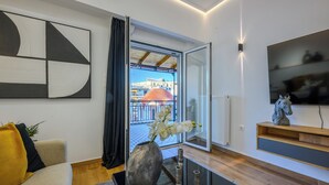 Un salón moderno con sofá, un jarrón con flores, televisión y un balcón con vistas a edificios.