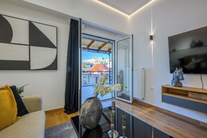 Ein modernes Wohnzimmer mit einer Couch, einem Blumenvasen, einem Fernseher und einem Balkon mit Blick auf Gebäude.